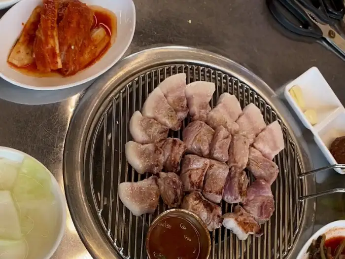 접시에 담긴 잘 익은 돼지고기 조각들. 곁들임 찬으로 김치와 쌈채소가 보인다.