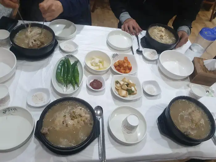 테이블에 놓인 여러 개의 삼계탕 뚝배기와 반찬들