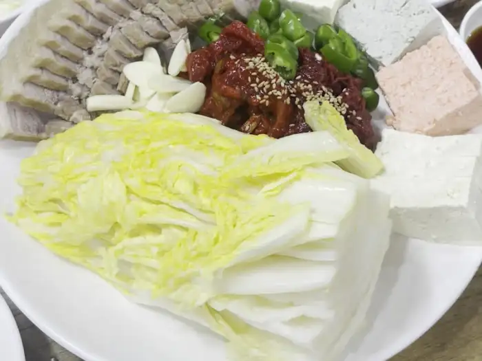 플레이팅된 음식의 클로즈업 샷. 삼색 두부와 쌈 채소, 양념 등이 부각되어 보임