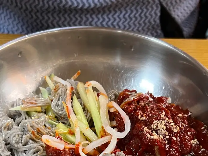 막국수 그릇의 일부가 클로즈업된 사진으로, 면과 양념, 그리고 고명이 보인다.