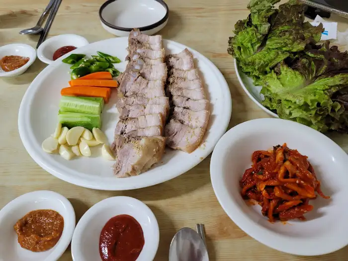 김이 모락모락 나는 수육과 신선한 쌈채소, 마늘, 쌈장, 새우젓 등이 정갈하게 차려진 모습.