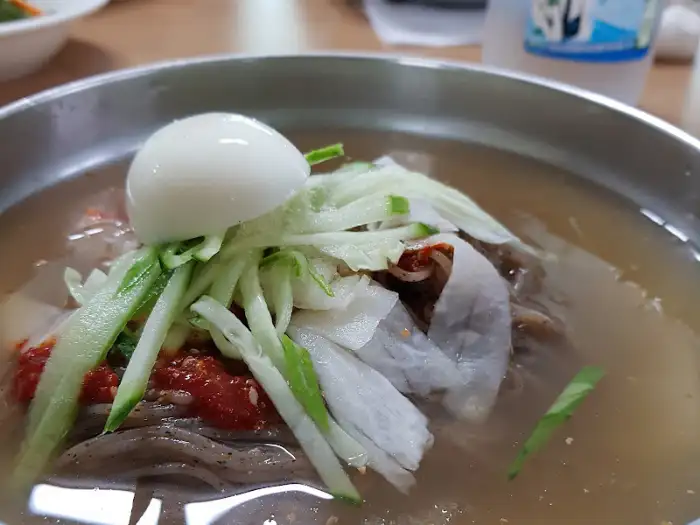 물막국수 그릇의 클로즈업. 국물 위에 삶은 계란, 채 썬 오이, 양념장이 보기 좋게 담겨 있다.
