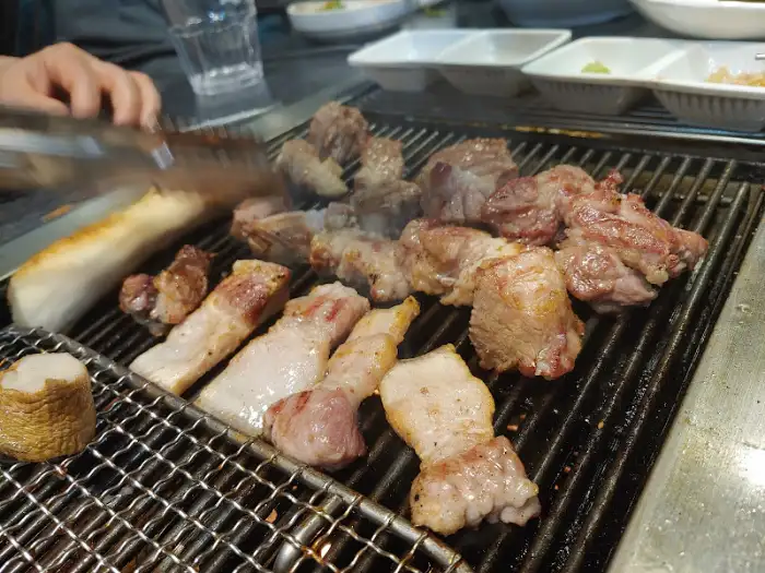목살 조각들이 불판 위에서 익어가고 있는 모습과 함께 곁들여진 떡 또는 빵 조각