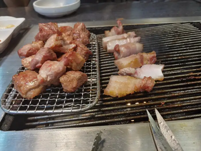 불판 위에 놓인 다양한 돼지고기 조각들과 곁들임 재료들