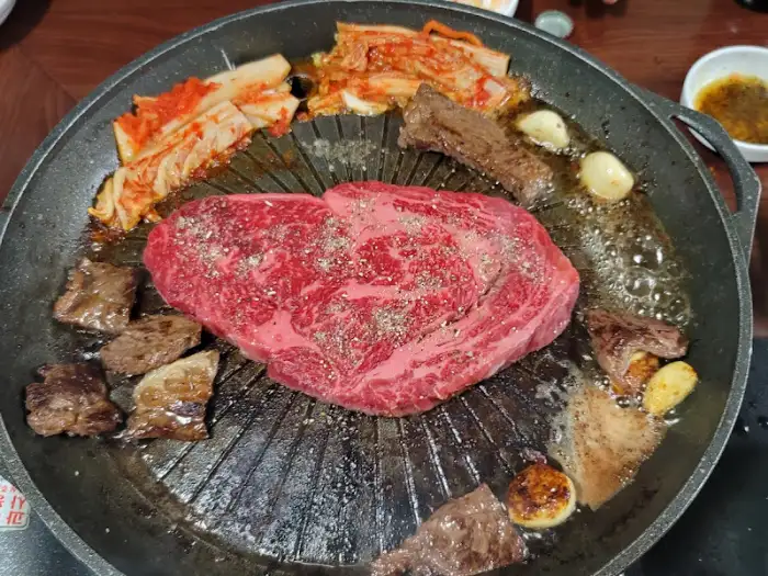 잘 달궈진 불판 위에 두툼한 등심과 김치, 마늘 등이 올라간 모습