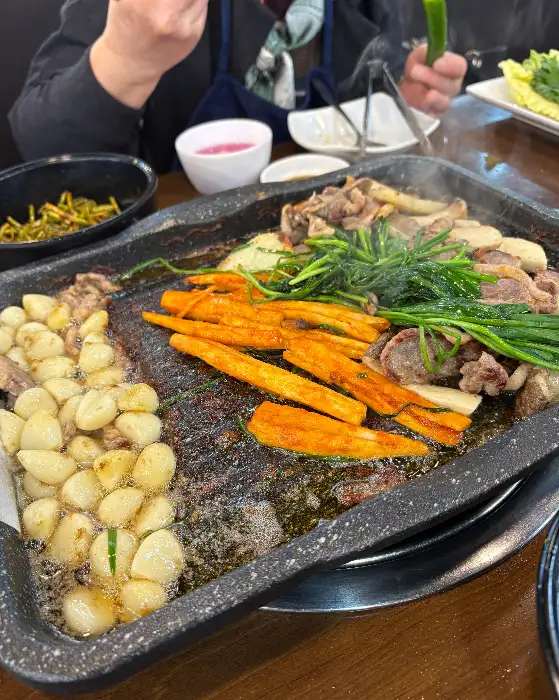 철판 위에서 잘 익은 오리고기와 마늘, 파릇한 채소가 어우러진 모습