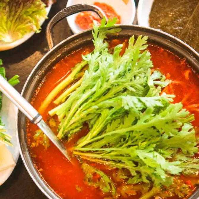 잘 차려진 식탁 위, 오리탕이 중앙에 놓여있고 주변으로 다양한 쌈 채소와 반찬들이 보입니다.