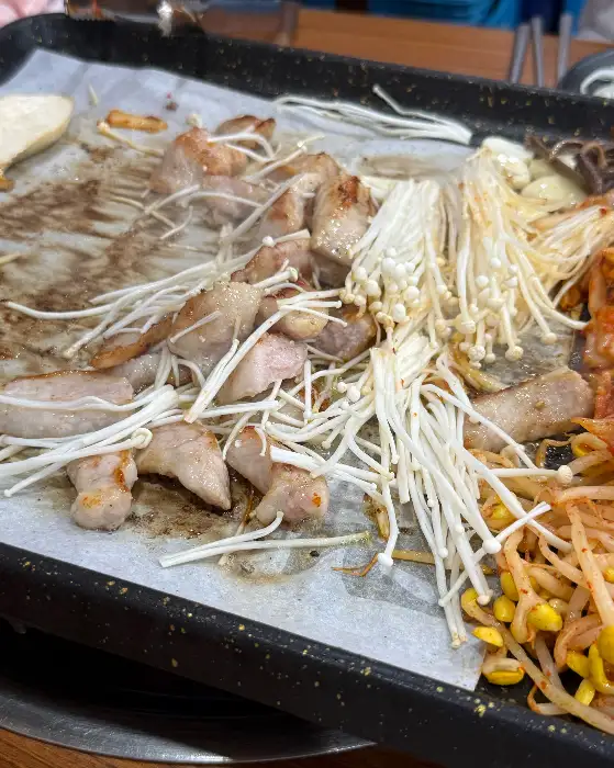 불판 위에서 구워지고 있는 삼겹살과 버섯, 콩나물, 고사리