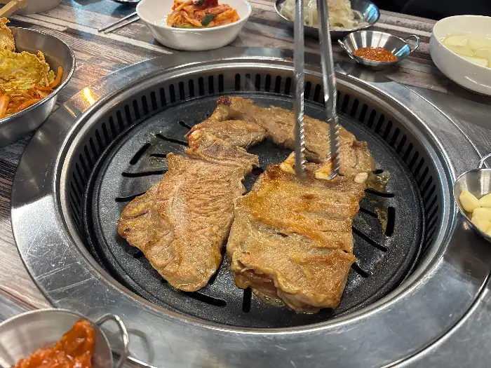 갈빗대가 있는 돼지갈비가 숯불 위에서 익어가고 있습니다. 집게로 집어서 뒤집는 모습입니다.