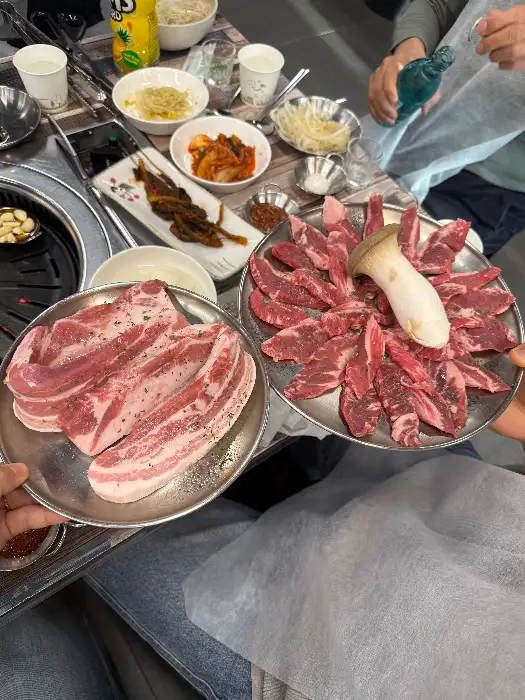다양한 쌈 채소와 함께 준비된 고기 한 접시. 왼편에는 두툼한 고기 덩어리가, 오른편에는 얇게 썰어진 고기들이 담겨 있습니다.