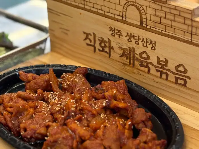 나무판에 적힌 '직화 제육볶음' 문구와 접시 위의 제육볶음