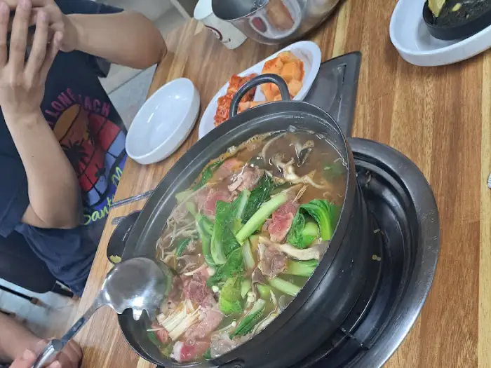 테이블 위에 놓인 샤브샤브 냄비와 손으로 국자를 들고 있는 사람