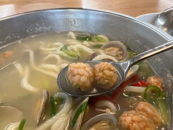 칼국수 위에 놓인 숟가락, 통통한 새우 완자와 바지락이 보입니다.