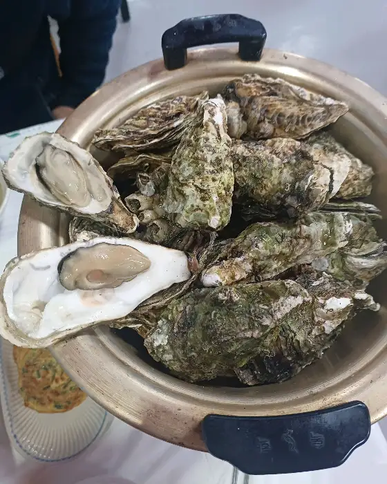 김이 피어오르는 굴찜 냄비와 껍질을 깐 굴