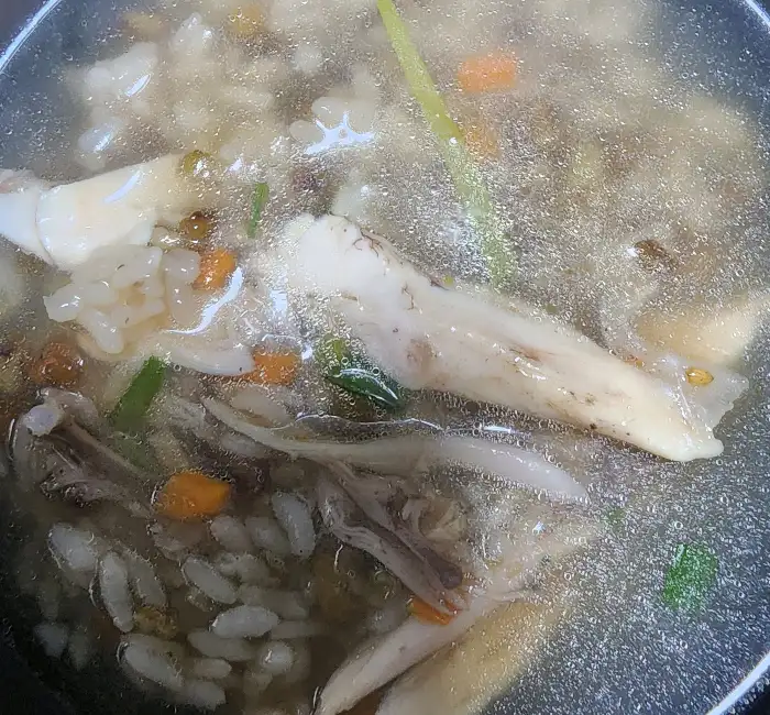 닭죽에 닭고기 살점과 쌀알, 채소가 보이는 모습