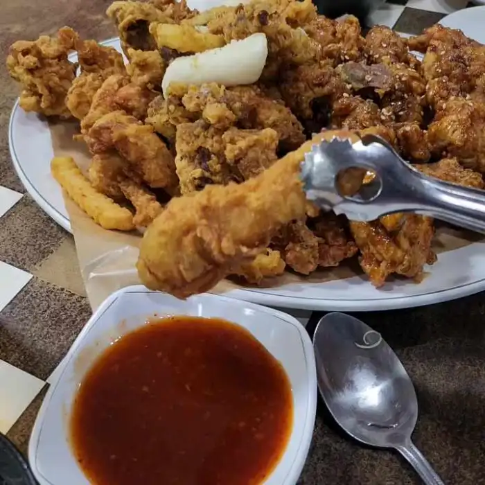 음식 사진 4: 집게로 후라이드 치킨 한 조각을 집어 소스에 찍어 먹는 모습