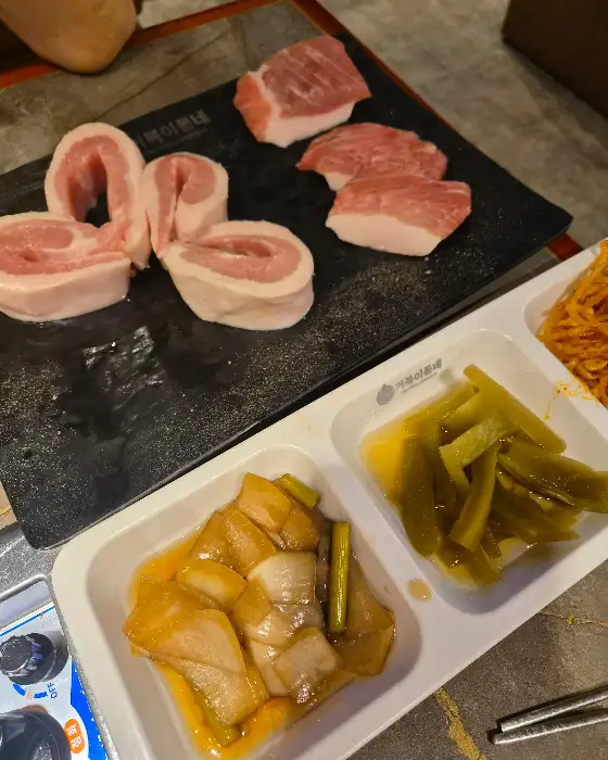 불판 위에서 맛있게 익어가는 삼겹살과 곁들임 반찬