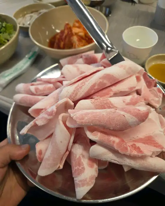 두툼하게 말린 냉동 삼겹살 덩어리가 접시에 담겨 있습니다.