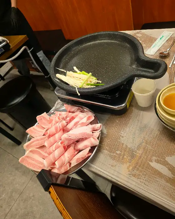 팬이 올려진 휴대용 버너와 그 옆에 놓인 냉동 삼겹살 접시.