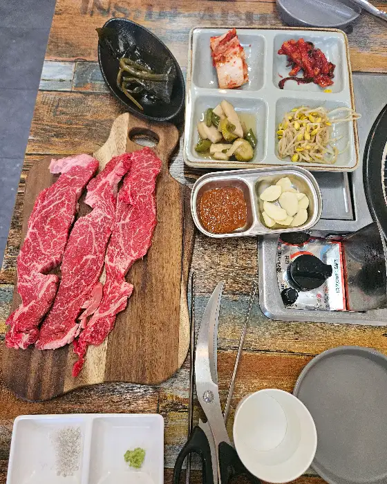 다양한 밑반찬과 신선한 고기가 함께 차려진 테이블 모습