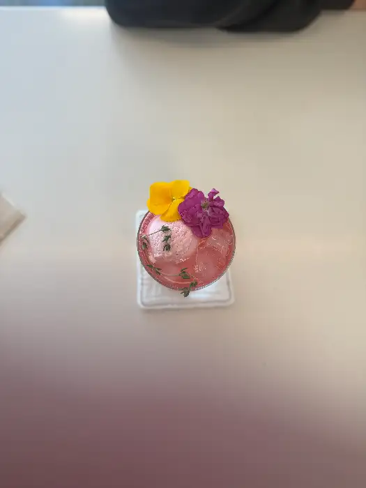 분홍색 음료에 꽃과 허브이 올려져 있는 모습