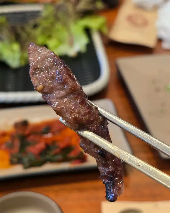 집게에 집힌 잘 구워진 소고기 한 점.