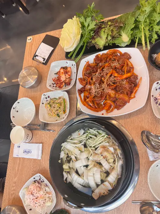 직화 제육, 낙지, 오징어 볶음과 다양한 쌈 채소, 곁들임 찬이 차려진 모습