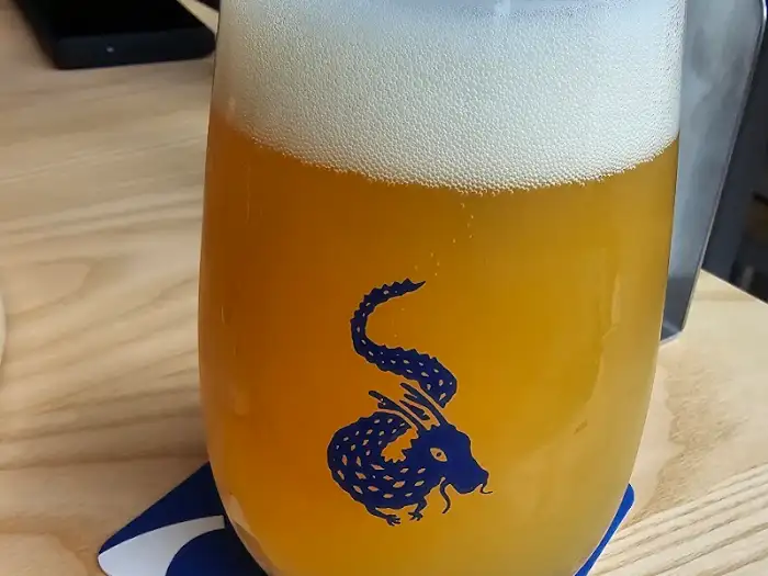 또 다른 맥주 잔, 잔에는 용 문양이 새겨져 있고 맥주는 풍성한 거품과 함께 담겨 있다.