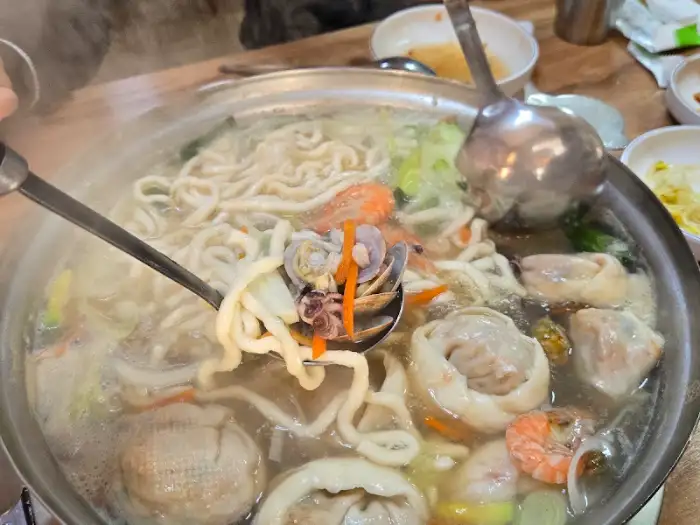 끓고 있는 해물칼국수 솥에 푸짐하게 담긴 해물과 면발