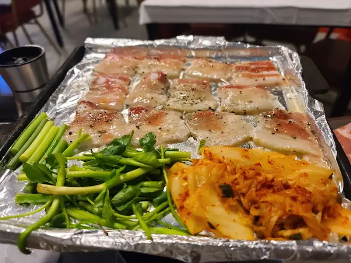 불판 위에서 노릇하게 익어가는 삼겹살과 미나리, 김치