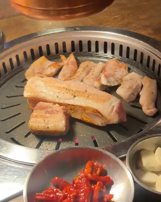 지글거리는 불판 위에서 익고 있는 오겹살과 곁들임 반찬들