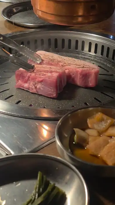 직원이 집게로 두툼한 고기를 불판 위에 올리고 있습니다.