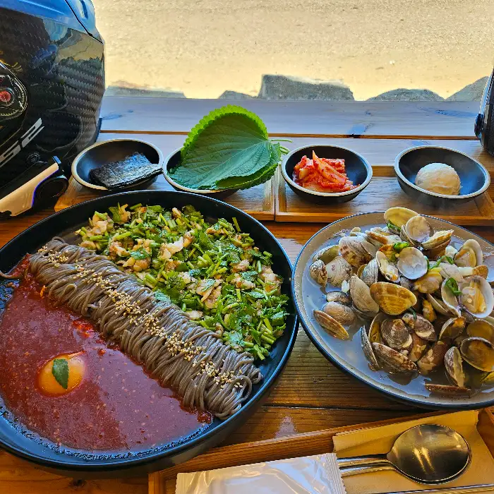 창가 테이블 위에 놓인 꼬막 한 판과 비빔 막국수