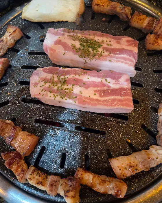 두툼한 삼겹살 두 덩이가 불판 위에서 맛있게 익어가는 모습