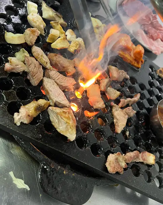 불판 위에서 맛있게 익고 있는 다양한 고기 조각들. 불꽃이 인상적입니다.