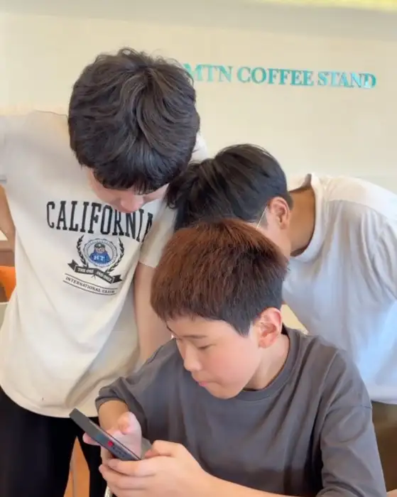 세 명의 남학생이 휴대폰을 보며 이야기하는 모습
