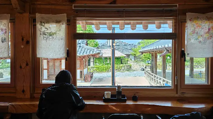 창밖으로 한옥 풍경이 보이는 자리에서 음료를 마시는 사람의 뒷모습.