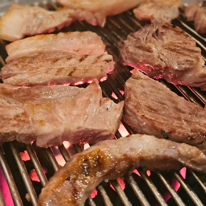 다양한 부위의 고기들이 연탄불 위에서 지글지글 익어가고 있습니다. 붉은 불꽃이 고기의 육즙을 가두는 듯합니다.