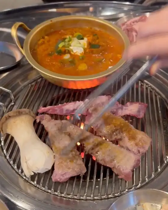 연탄불 위에서 익어가는 다양한 부위의 고기들과 함께 곁들임 메뉴가 푸짐하게 차려져 있습니다.