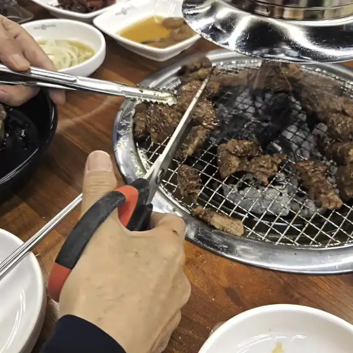 가위와 집게로 먹기 좋게 자르고 있는 갈비