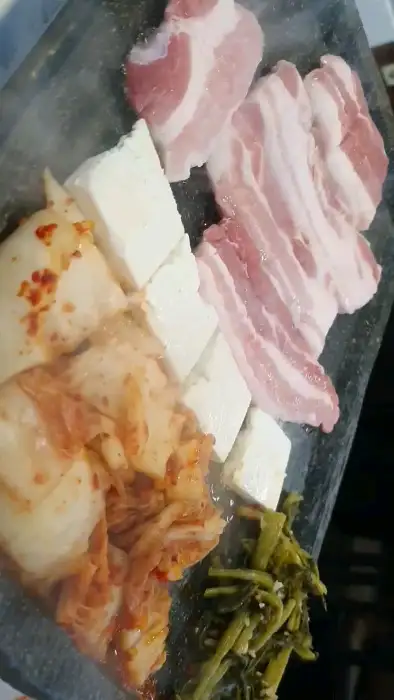 두툼하게 썰어진 삼겹살, 김치, 두부가 불판 위에서 구워지는 모습