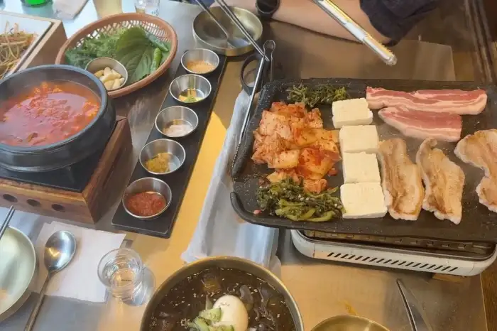 테이블 위에 놓인 식사 준비 상태. 냄비, 불판, 밑반찬, 소스 그릇 등이 보인다.