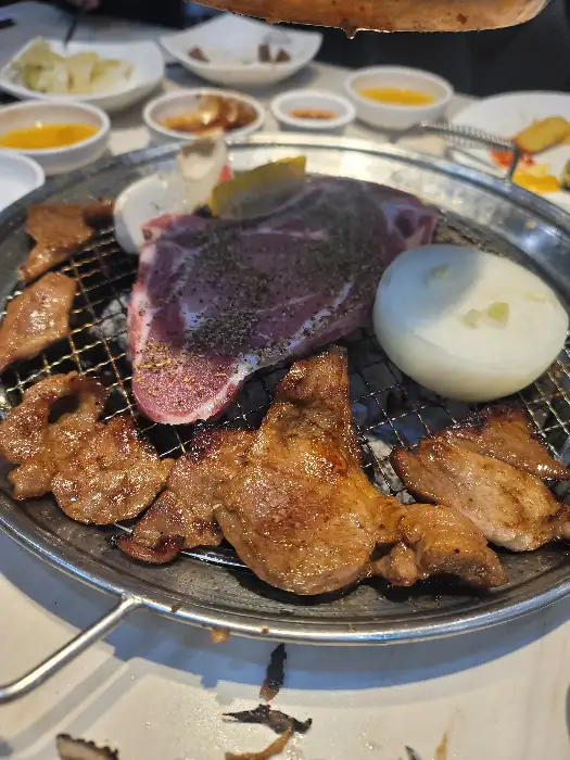 숯불 위에 올라간 두툼한 고기 덩어리와 양파, 마늘.