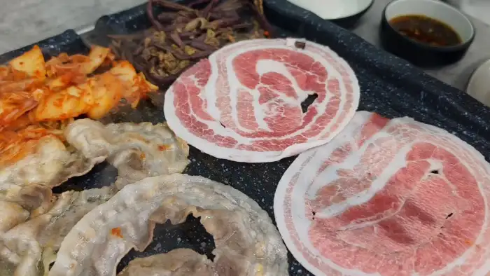 불판에 지글지글 익어가는 삼겹살과 김치, 콩나물이 먹음직스럽게 보인다.