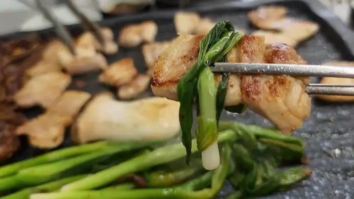 집게로 집어 올린 고기가 파와 함께 맛있게 익은 모습.