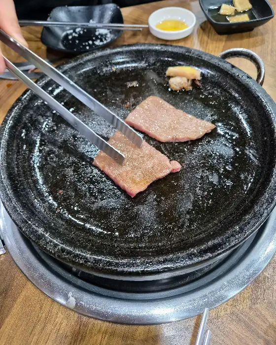 집게로 석쇠 위 고기를 뒤집는 모습