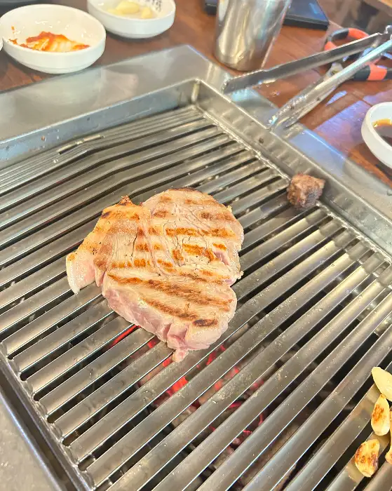 잘 구워진 삼겹살 한 점이 불판 위에서 지글거리는 모습