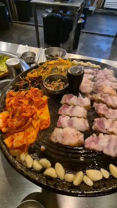 솥뚜껑 불판 위에서 지글지글 익어가는 삼겹살과 김치, 파절이의 모습
