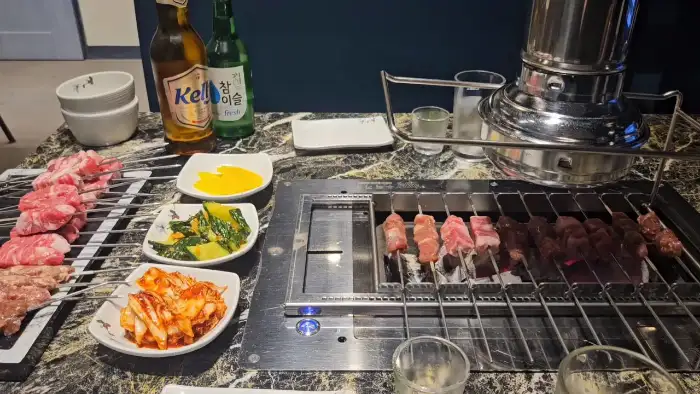 테이블에 놓인 양꼬치, 곁들임 반찬, 맥주 및 소주병