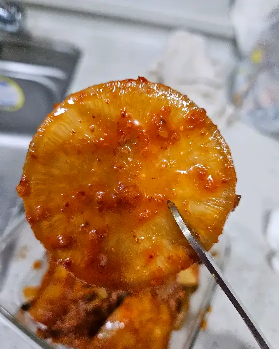 두툼한 깍두기 한 조각을 집게로 집고 있는 모습. 빨간 양념이 먹음직스럽습니다.